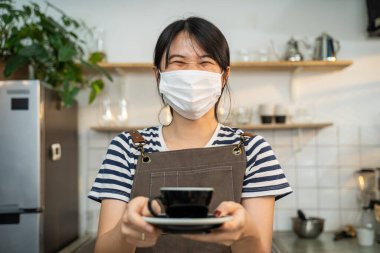 Tanınmayan Garson standını kapatın ve kafede iki eli olan müşteriye bir fincan sıcak kahve verin. Restoran işletmecisi önlüklü kız barista insanlara hizmet veriyor.