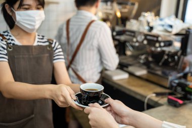 Tanınmayan Garson standını kapatın ve kafede iki eli olan müşteriye bir fincan sıcak kahve verin. Restoran işletmecisi önlüklü kız barista insanlara hizmet veriyor.