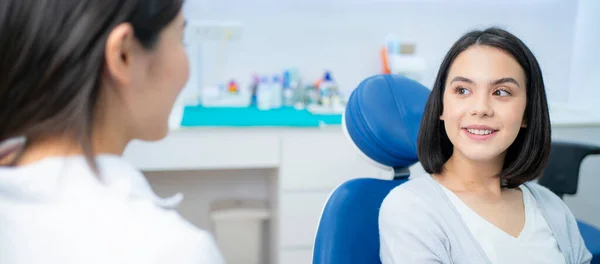 在牙科诊所的牙齿护理计划中 白人美女与亚洲女牙医就蛀牙和牙龈疾病进行了交谈和咨询 年轻女人很高兴得到专业牙医的照顾 — 图库照片