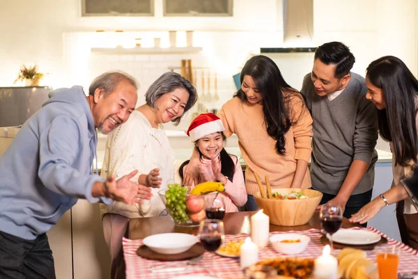 Happy family time and relationship, Asian big family having small Christmas party eating food together at home. Kid is happy to see parent, cousin preparing food and bring it to dining table at home.