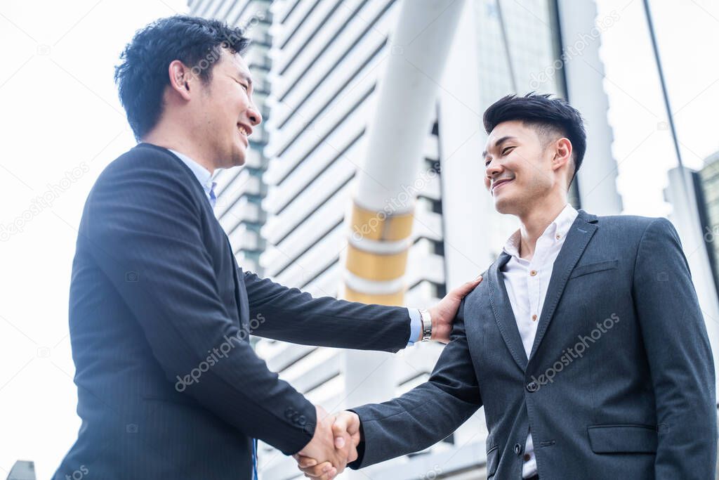 Asian businessman making handshake in the city building in the background. A partnership agreement is successful after complete the negotiation. Business deal, merger and acquisition concepts.