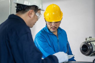 Asyalı mekanik işçiler değirmen makinesinde çalışıyor. Güvenlik önlemi için makineyi çalıştırırken koruyucu gözlük ve kask takan teknisyenler. Lider, ekip üyesine bir iş yapmasını tavsiye ediyor