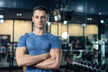 Spor kıyafetleri içinde altı paket karın kası olan sporcu portresi. Kolları çapraz duruyor. Sonra spor salonundaki kameraya bakın. Vücut geliştirme kaslı adam fitness kulübünde sağlık için egzersiz yapıyor..