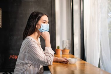 Kafkasyalı güzel kadın müşteri Covid 19 salgınından dolayı yüz maskesi takıyor. Mesafeyi koruyor. Kafeteryada tek başına oturuyor. Genç çekici kız rahatla ve kahveciden bir fincan kahve iç.