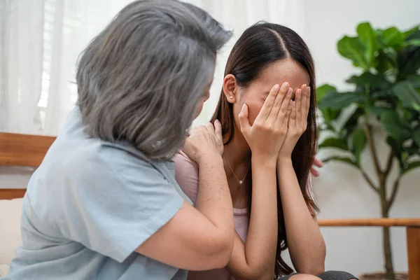 Asian loving elderly mother consoling and comforting upset depressed young girl daughter crying for problem. Caring Senior mom support and understanding empathy to stressed woman in tears at home.