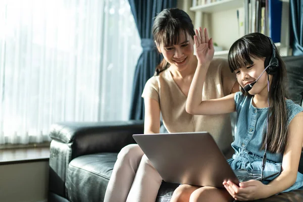 家喻户晓的亚洲小女生由于眼镜蛇的流行 通过远程会议从学校老师那里学习虚拟互联网在线课程 慈爱的母亲用手提电脑教和支持女儿 — 图库照片