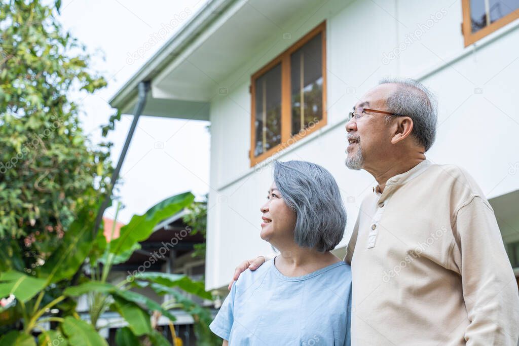 Asian Senior elderly couple standing outdoor at house feeling happy and enjoy retirement life together. Loving Older grandparent smile and hugging each other. Relationship and activity at home concept