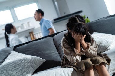 Asyalı kız çocuk evde kavga ederken ya da kavga ederken kanepede oturup ağlıyor. Yüzü ve gözleri ellerle kaplayan çocuk şiddeti görmek istemiyor. Ailede aile içi sorunlar