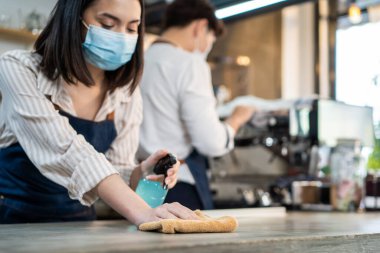 Kafe garsonu maske takıyor, mağazayı açmak için dezenfektanlı temiz bir restoran. Asya kökenli genç çift, Covid19 kilitlenmesinden sonra dükkanı yeniden açmadan önce restoranda dezenfekte, temizleme ve ovalama yapıyor..