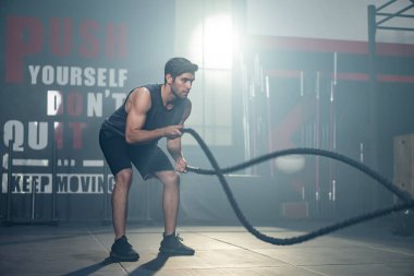 Kafkas genç aktif yakışıklı sporcu spor salonunda spor yapıyor. Çekici sporcu kaslı erkek antrenmanı. Savaş halatı kullanarak kilo vermek ve spor salonunda kas yapmak için çifte dalga oluşturur..