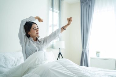 Pijamalı Asyalı güzel kız sabah mutlulukla uyanıyor. Çekici genç bir kadın gülümsüyor, mutlu ve rahat hissediyor. Sonra da yatak odasında uyuduktan sonra vücudunu esnetiyor..