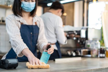 Kafe garsonu maske takıyor, mağazayı açmak için dezenfektanlı temiz bir restoran. Asya kökenli genç çift, Covid19 kilitlenmesinden sonra dükkanı yeniden açmadan önce restoranda dezenfekte, temizleme ve ovalama yapıyor..