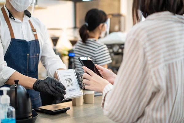 Covid19 salgını sırasında Asyalı kadın müşterilere hızlı ve kolay bir ödeme yapıyorlar. Genç kız servis ücretini ödemek ve garson garsondan içmek için akıllı telefon tarama kodu kullanıyor..