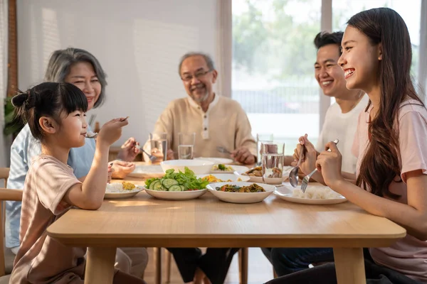 Big Asian happy family spend time having lunch on dinner table together. little kid daughter enjoy eating food with father, mother and grandparents. Multi-Generation relationship and activity in house