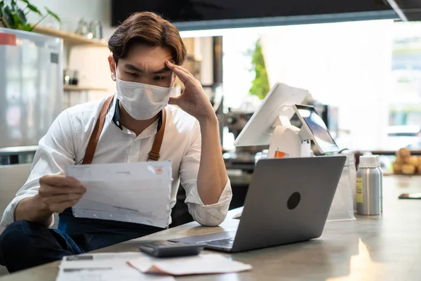 Asyalı kafe sahibi faturalar ve iş ödemeleri yüzünden hayal kırıklığına uğramış görünüyor. Depresyondaki barista çalışanı Covid19 salgını sırasında koruyucu maske takıyor. Restorandaki finansal problemden endişe ediyor..