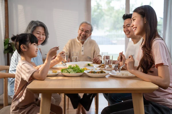 Asyalı mutlu aile yemek masasında öğle yemeği yiyor. Küçük kız, baba, anne ve büyükbaba ile birlikte yemek yemekten hoşlanıyor. Evde çok nesilli ilişki ve aktivite