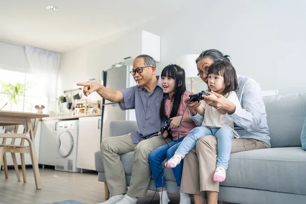 Asian happy family stay home grandparent play game with little girl. Loving senior elder older couple play video games in front of television with young children granddaughter in living room together.