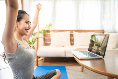 Covid-19 salgınından dolayı Asyalı genç ve güzel bir kız evde egzersiz yapıyor. Aktif spor kadını evdeki tecrit aktivitesinden zevk alıyor, Yoga yaparak egzersiz yapıyor, Pilates online eğitmenin talimatlarını takip ediyor..
