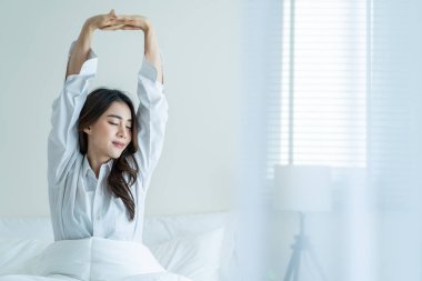 Pijamalı Asyalı güzel kız sabah mutlulukla uyanıyor. Çekici genç bir kadın gülümsüyor, mutlu ve rahat hissediyor. Sonra da yatak odasında uyuduktan sonra vücudunu esnetiyor..