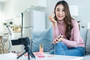 Asyalı vlogger 'ın portresi evdeki kozmetik incelemeden sonra kameraya bak. Güzel blogcu Nüfuzlu Kız kanepeye oturur ve canlı yayında izleyicilere makyaj malzemelerini gösterir.