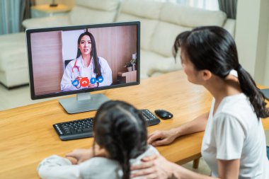 Asyalı sevgili anne ve küçük kız doktorla görüntülü görüşme. Çekici pediyatrist sanal internet için dizüstü bilgisayar kullanır. Oturma odasında küçük çocuklara ve ailelerine sağlıkları için danışmanlık ve tedavi uygular..