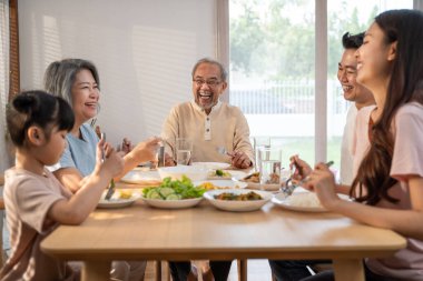 Asyalı mutlu aile yemek masasında öğle yemeği yiyor. Küçük kız, baba, anne ve büyükbaba ile birlikte yemek yemekten hoşlanıyor. Evde çok nesilli ilişki ve aktivite