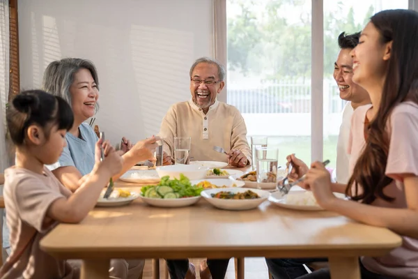 Asian Big happy family spend time have lunch on dinner table together. Little kid daughter enjoy eating foods with father, mother and grandparents. Multi-Generation relationship and activity in house