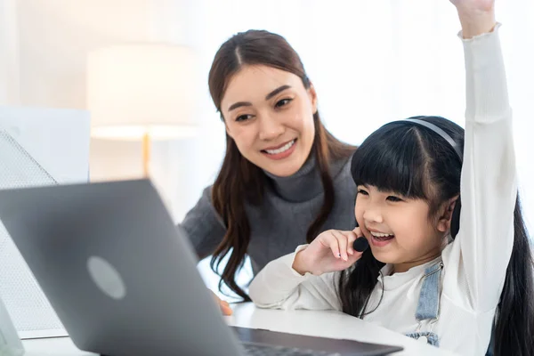 Asyalı küçük kız evde annesiyle online ders alıyor. Anaokulu çocuğu dizüstü bilgisayar kullanır ev ödevi yapar, okul öğretmeninden dijital uzaktan internete geçer ve annesinden destek alır..