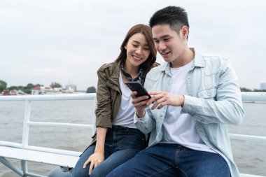 Teknede oturan çift akıllı telefona bakıyor.