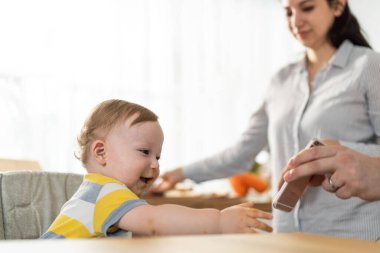 Bebek akıllı telefona uzanırken kadın yakınlarda duruyor.