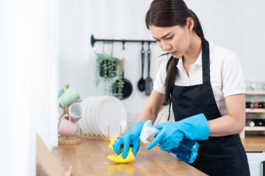 Kadın mutfak tezgahını sünger ve sprey kullanarak temizliyor.