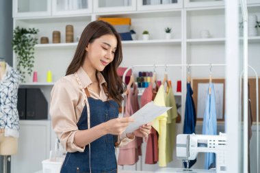 Asyalı terzi kadının portresi terzi atölyesinde giysiler üzerinde çalışıyor.