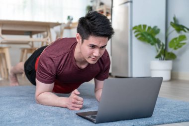 Asyalı yakışıklı aktif genç adam oturma odasında yerde egzersiz yapıyor.