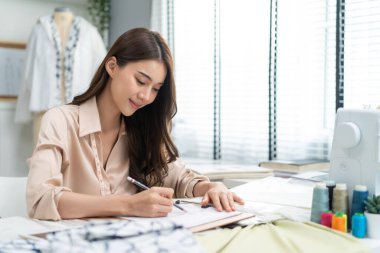 Dikiş masasında oturan kadın notlar yazıyor.