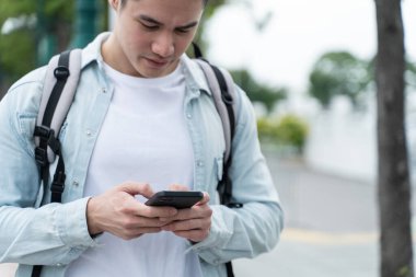 Adam ağaçların yanında dikilirken akıllı telefon kullanıyor.