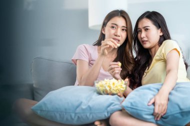 İki kadın kanepede oturup patlamış mısır yiyor.