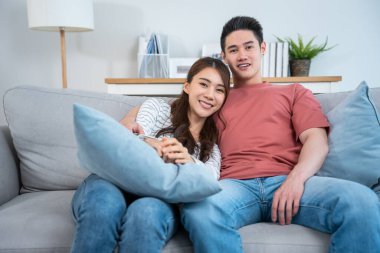 Çift kanepede birlikte oturup yastık tutuyor ve gülümsüyor.