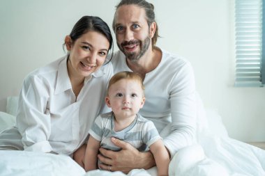 Gülümseyen aile çocuklarıyla birlikte yatakta oturuyor.