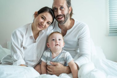 Gülümseyen aile yatakta yan yana oturuyor.