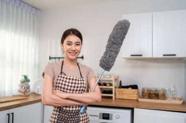 Gülümseyen kadın elinde toz bezi, modern mutfakta duruyor.