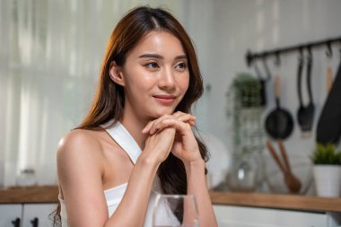 Masada oturmuş, elleri birbirine kenetlenmiş gülümseyen bir kadın.