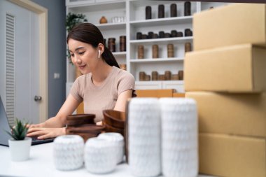 Dizüstü bilgisayarda çalışan kadın paketleme malzemeleri ve bitkilerle çevrili.