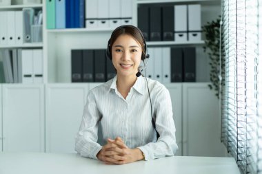 Ofis masasında oturan, kulaklık takan gülümseyen kadın.