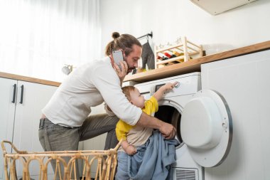 Çamaşır makinesine çamaşır koyarken telefonu tutan adam