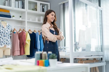 Asyalı terzi kadının portresi terzi atölyesinde giysiler üzerinde çalışıyor.
