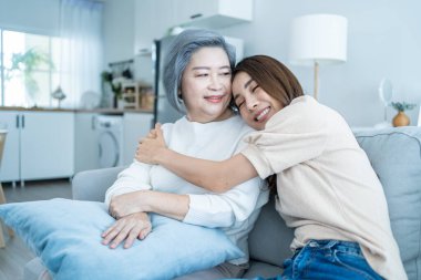 Mutlu Asyalı son sınıf öğrencisi kadın torununa sarılıyor ve evde gülümsüyor.