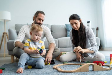 Aile, renkli oyuncaklarla yerde birlikte oynuyor.