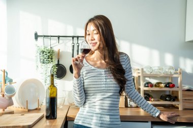 Kadın modern mutfakta dururken kırmızı şaraptan zevk alıyor.
