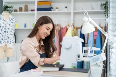 Asyalı güzel terzi kadın terzi atölyesinde giysiler üzerinde çalışıyor..