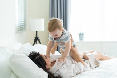 Anne bebeğiyle yatakta neşeyle oynuyor.